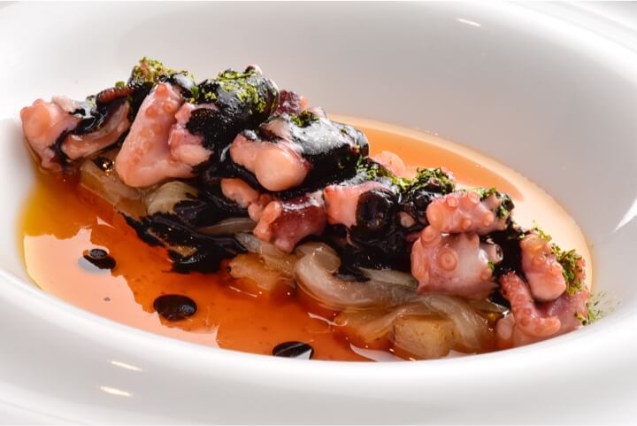 Pulpo bebé com cebollas caramelizadas e patatas rotas servido en el restaurante The White Box en hot